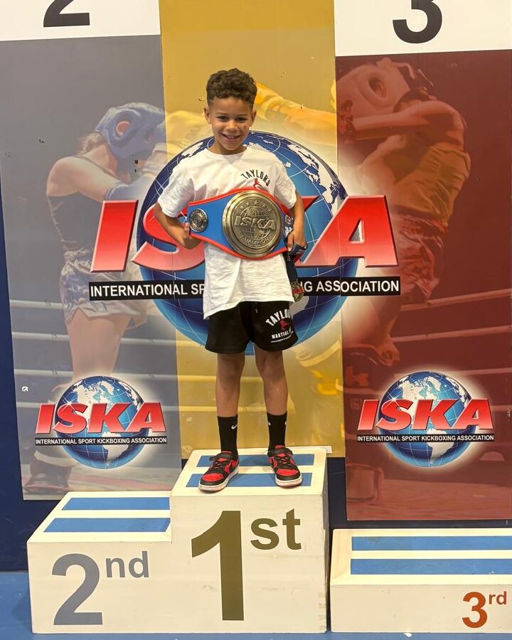 A young Taylor's Martial Arts student on the first place podium holding an ISKA champion belt