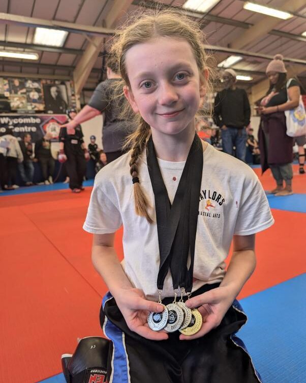 A young Taylor's Martial Arts student holding four competition medals