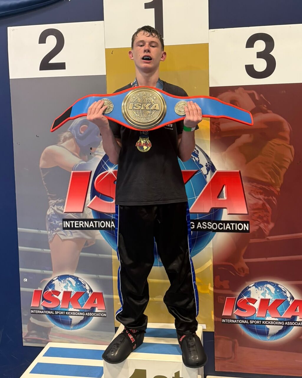 A teenage Taylor's Martial Arts student on the first place podium holding an ISKA champion belt
