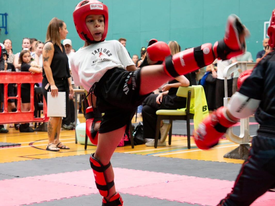 Kids kickboxing at Taylor's Martial Arts A young Taylor's Martial Arts student throwing a high roundhouse kick at a kickboxing competition