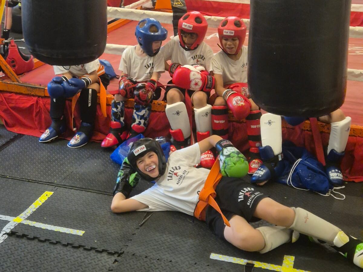 Kidzone class at Taylor's Martial Arts Young Kidzone students in headguards and shin pads resting ringside in Taylor's Martial Arts kit